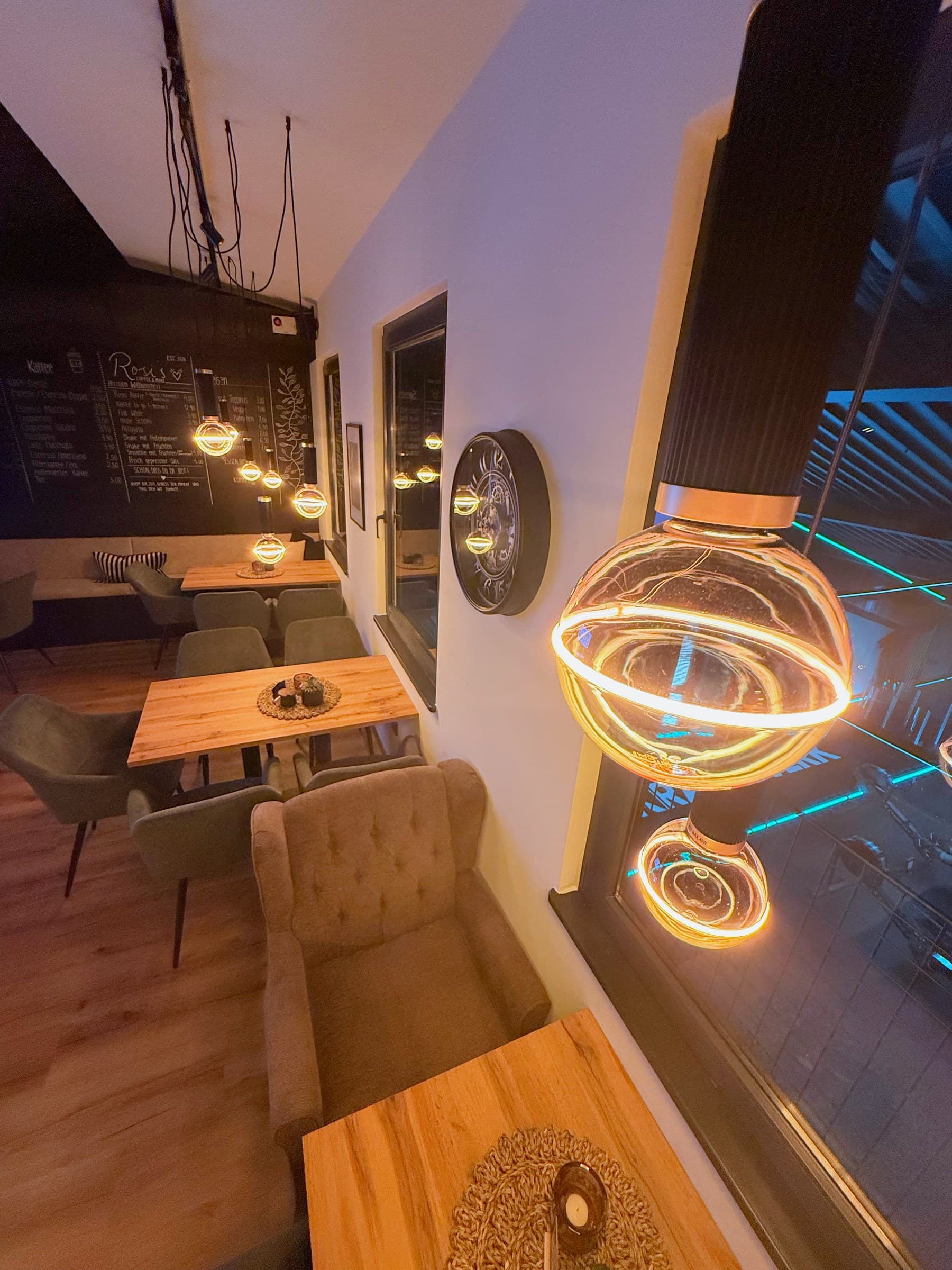 Sitzbereich mit Holztischen, Sesseln und Kreidetafel an der Wand