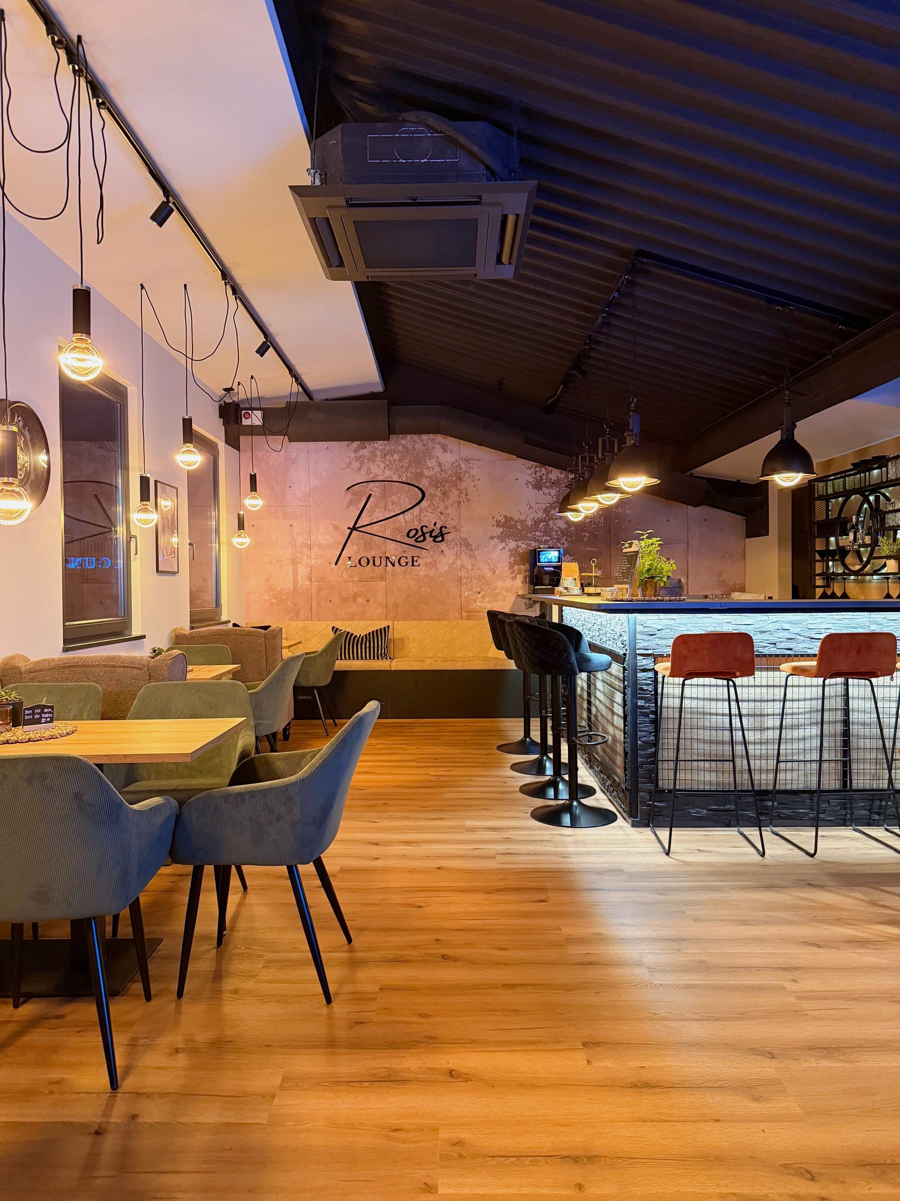 Rosi's Lounge mit Sitzplätzen, Theke und Schriftzug an der Wand